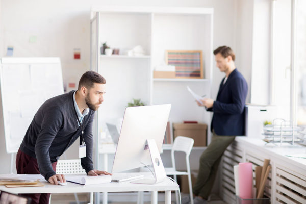 Side view portrait of bearded entrepreneur using computer standing at desk, copy space